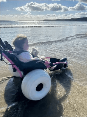 A Hippocampe beach wheelchair with large balloon tyres in the shallow sea, a child looking out towards the horizon